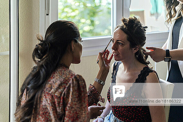 Make-up artist applying eyeshadow and hairdresser making hairstyle to customer at home