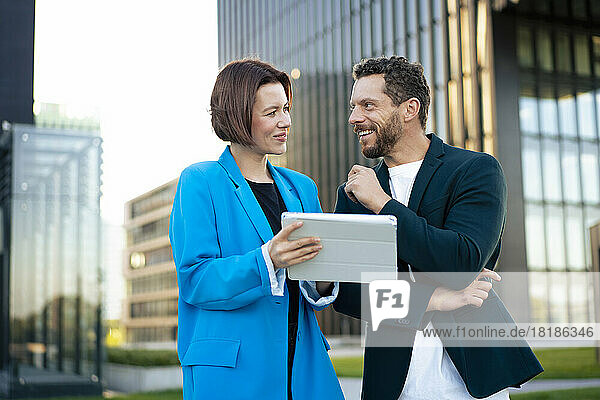 Smiling businessman looking at colleague holding tablet PC