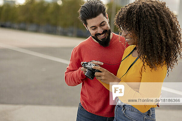 Happy young man with girlfriend holding camera at footpath