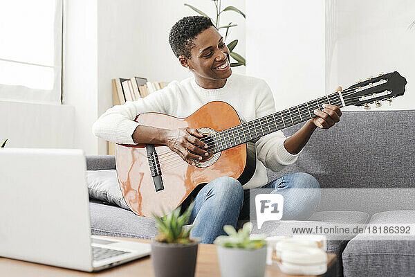Woman playing guitar on couch with laptop on table