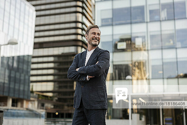 Smiling businessman standing with arms crossed outside office building