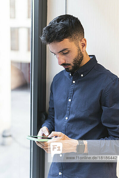 Young businessman using smart phone by window