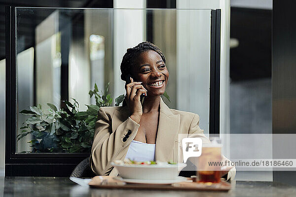 Happy businesswoman talking on mobile phone sitting at cafeteria