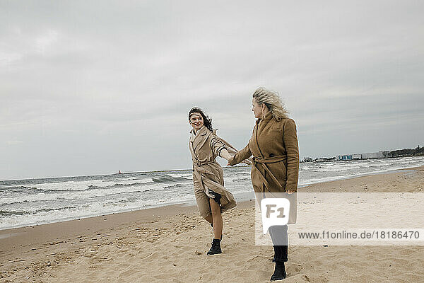 Mutter und Tochter stehen Händchen haltend am Strand