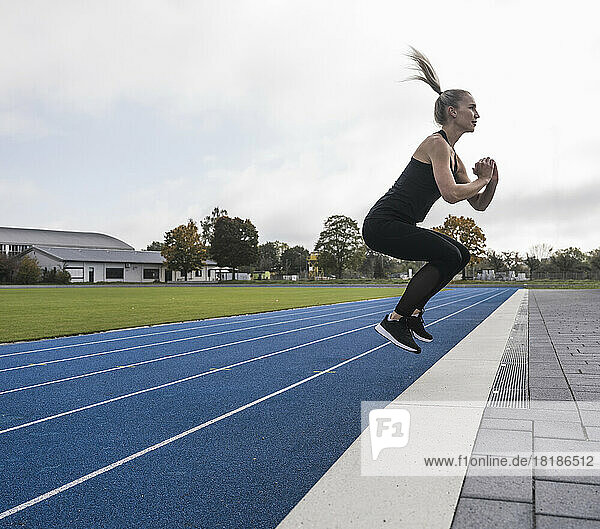 Young athlete doing jumping exercise on track