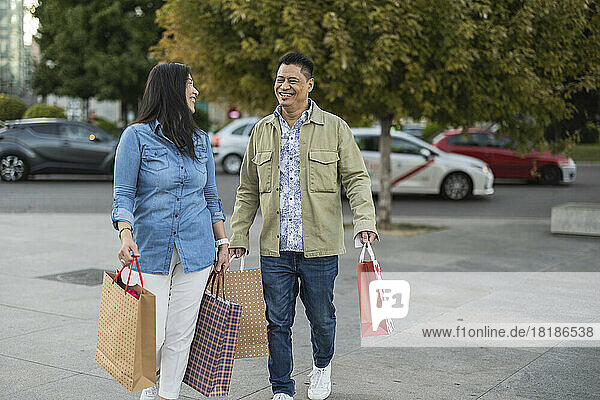 Glückliches älteres Paar mit Einkaufstüten  das auf dem Fußweg läuft