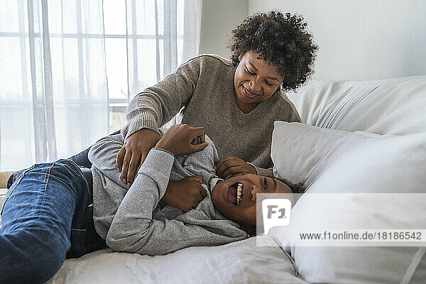 Playful mother ticking son on bed at home