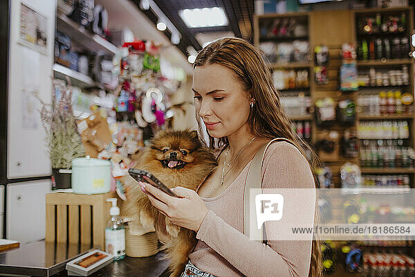 Woman carrying dog using smart phone in pet shop