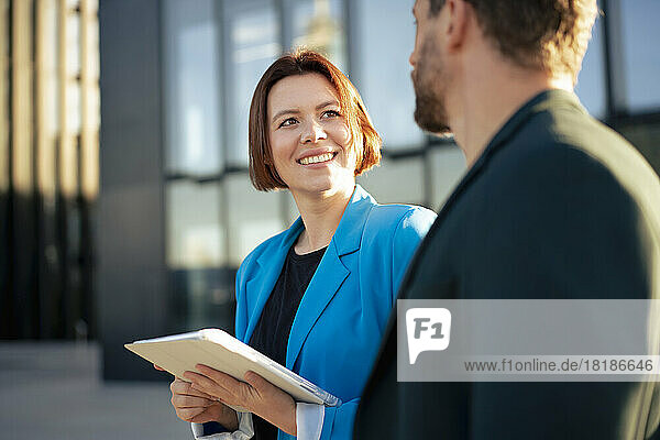 Smiling businesswoman with tablet PC looking at colleague on sunny day