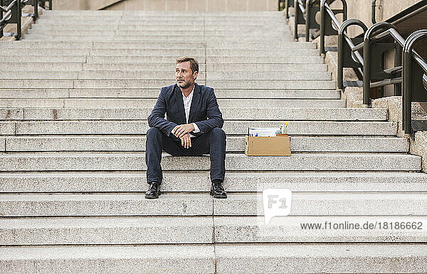 Trauriger Geschäftsmann sitzt mit Karton auf der Treppe