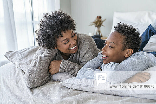 Happy mother and son having conversation lying on bed at home