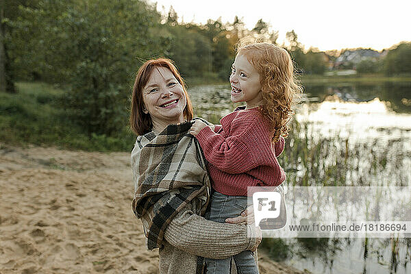 Happy woman carrying granddaughter near lake