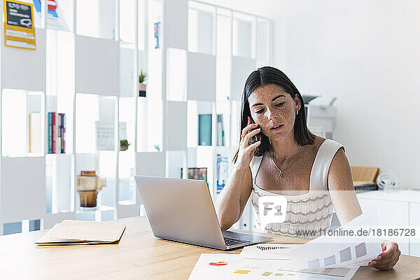 Young businesswoman discussing document on smart phone in office