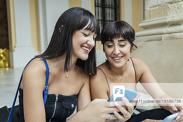 Smiling woman sharing mobile phone with friend