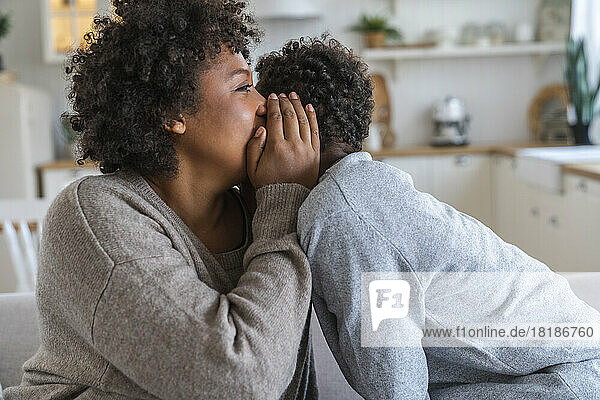 Mother whispering in son's ear at home