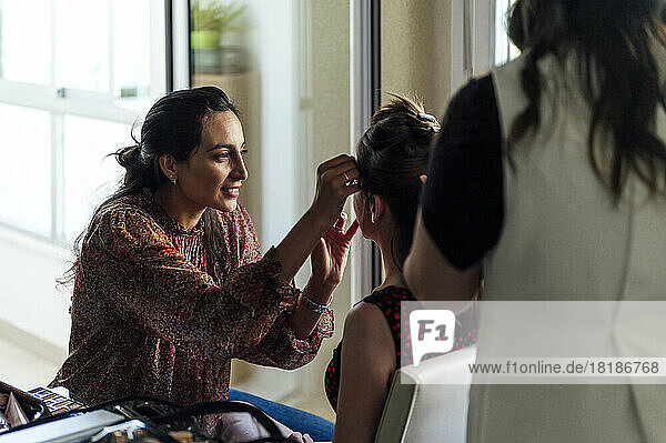 Smiling make-up artist applying eyeshadow to customer and hairdresser standing behind