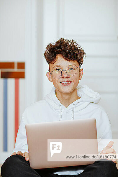 Smiling boy sitting with laptop at home