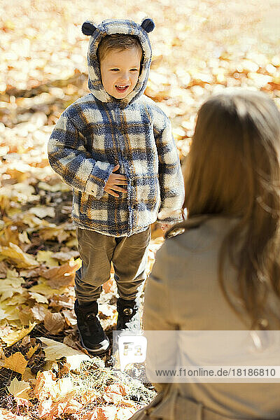 Cute boy wearing hooded jacket looking at mother in park