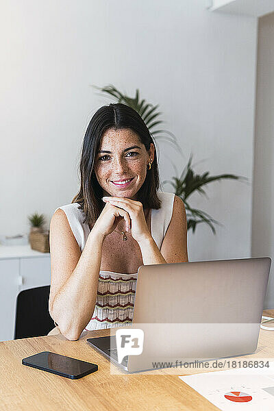 Happy young businesswoman sitting in front of laptop at office