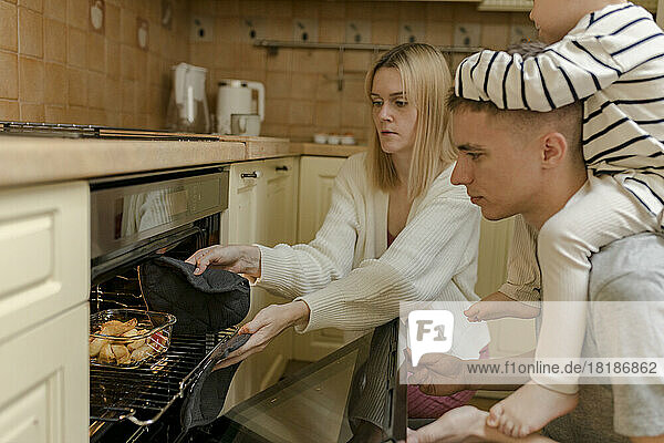 Vater und Sohn mit Mutter nehmen in der heimischen Küche Essen aus dem Ofen