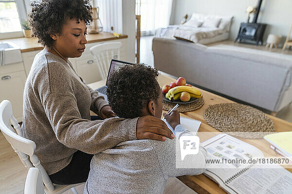 Mother helping son studying on table at home