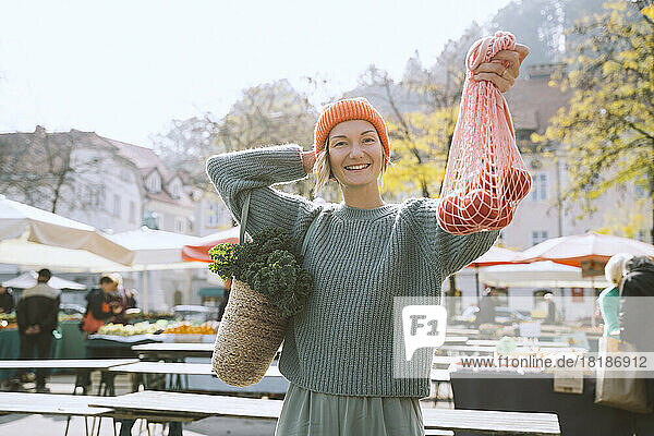 Smiling woman showing tomatoes in mesh bag at market