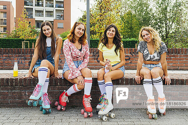 Smiling friends in roller skates sitting on wall