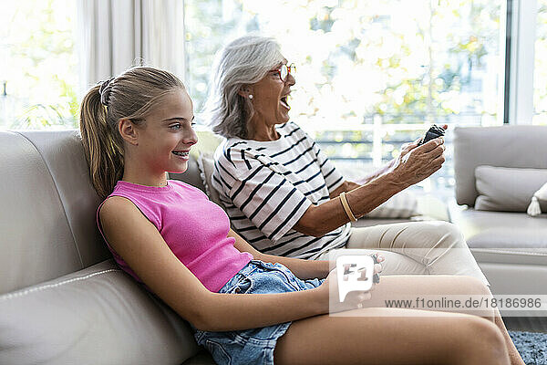 Grandmother and granddaughter enjoying playing video game sitting on sofa at home