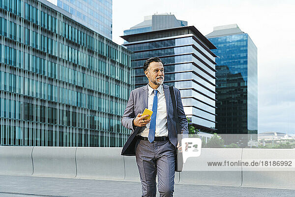 Thoughtful mature businessman with mobile phone walking on street