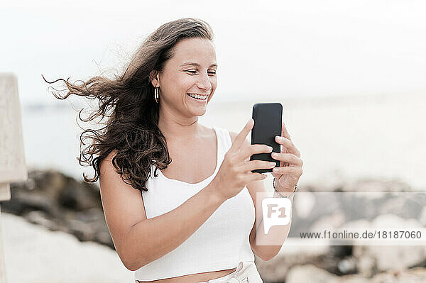 Lächelnde Frau fotografiert am Wochenende mit ihrem Smartphone am Strand