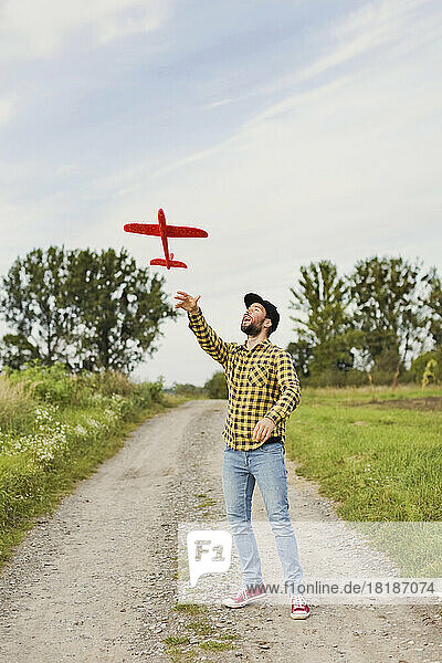Playful man flying toy airplane on dirt road