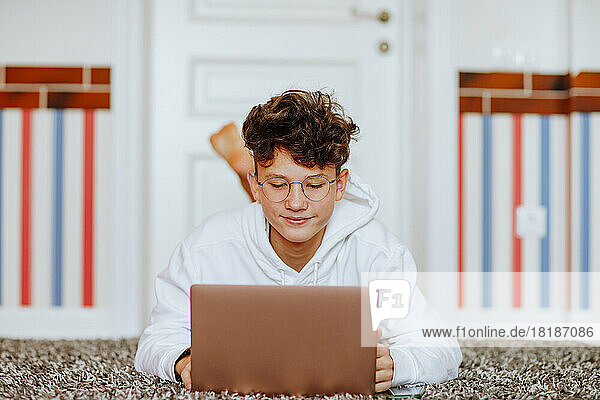 Smiling boy lying on carpet in front of laptop at home