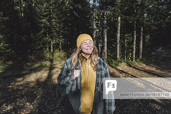 Glückliche Frau mit geschlossenen Augen beim Wandern im Wald an einem sonnigen Tag