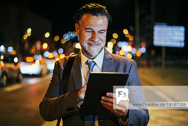 Glücklicher reifer Geschäftsmann  der nachts einen Tablet-PC nutzt