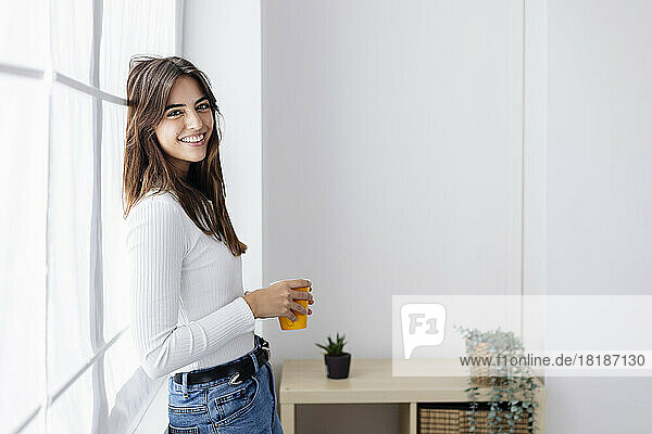 Happy woman holding coffee cup leaning on window