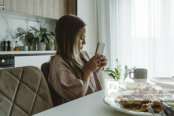 Girl photographing breakfast on table through smart phone at home
