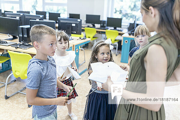 Students showing homework to teacher in classroom at school