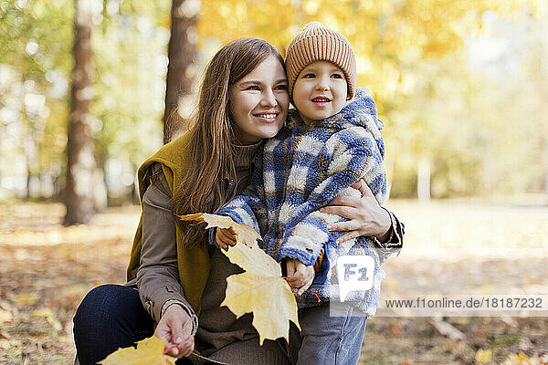 Cute boy with mother holding yellow leaves in park