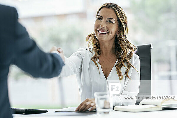 Glückliche Geschäftsfrau schüttelt ihrem Kollegen im Büro die Hand