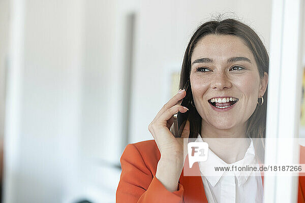 Glückliche Geschäftsfrau  die im Büro mit dem Mobiltelefon spricht und durch Glas gesehen wird