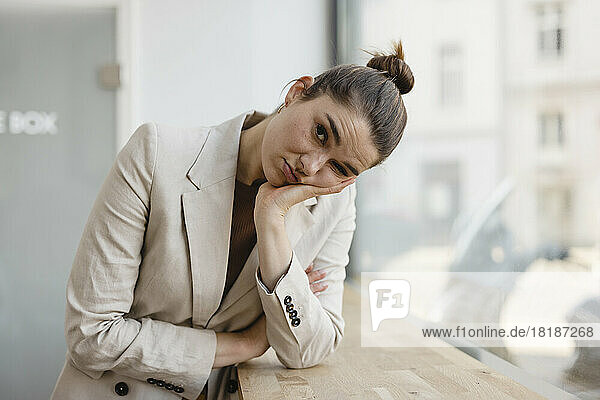 Bored businesswoman with head in hand by window at office