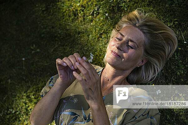 Smiling mature woman lying down holding flower in garden