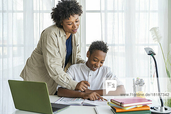 Mother assisting son studying at table in home
