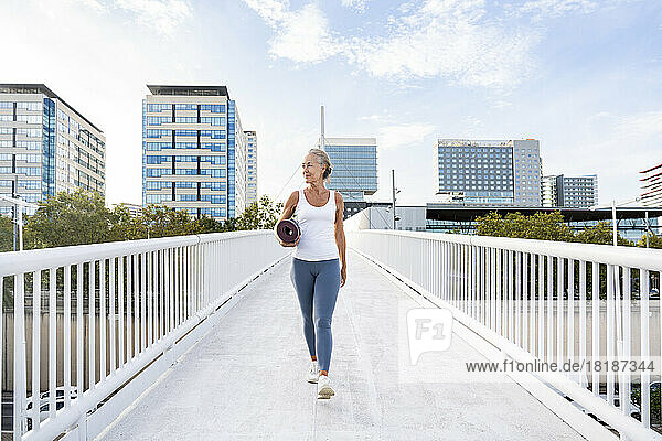 Woman holding exercise mat walking on footbridge