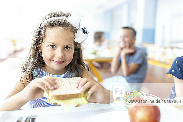 Smiling girl holding sandwich in school cafeteria