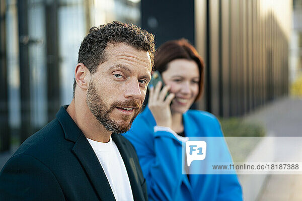Smiling businessman with colleague in background talking on smart phone