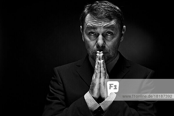 Mature man in full suit praying against black background  close up