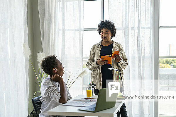 Mother with book helping boy studying at home