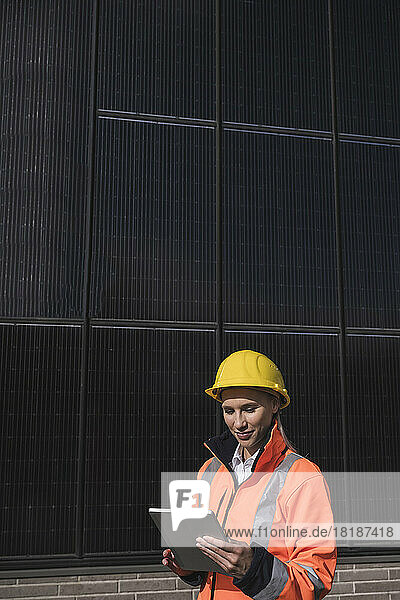 Junge Ingenieurin mit Schutzhelm und Tablet-PC vor Sonnenkollektoren