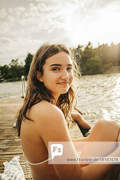 Seitenansicht einer lächelnden Frau  die im Urlaub auf einem Steg am See sitzt